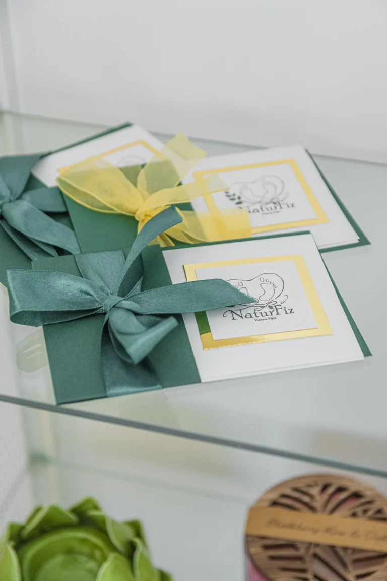 Eleganckie vouchery prezentowe NaturFiz z zielonymi i żółtymi kokardami, ułożone na szklanej półce.