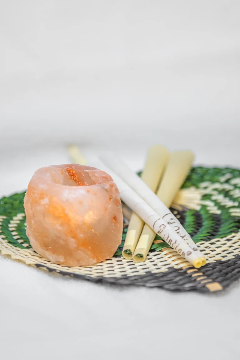 Naturalny świecznik solny i świece do świecowania uszu ułożone na plecionym podkładzie.